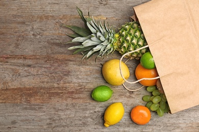 Photo of Paper bag with fresh tropical fruits on wooden background