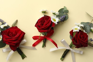 Many stylish red boutonnieres on beige background, flat lay