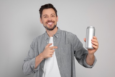 Happy man holding tin can with beverage on light grey background