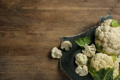 Photo of Cut and whole cauliflowers on wooden table, top view. Space for text
