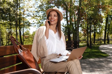 Photo of Woman talking on phone while working with laptop in park