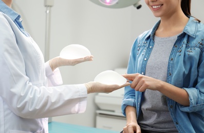 Photo of Doctor showing silicone implants for breast augmentation to patient in clinic, closeup. Cosmetic surgery