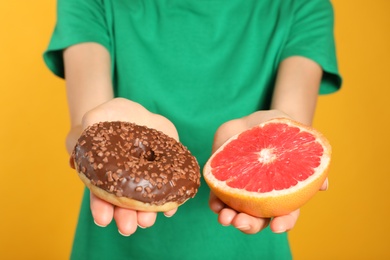 Photo of Woman choosing between doughnut and healthy grapefruit on yellow background, closeup
