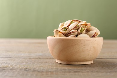 Tasty pistachios in bowl on wooden table against olive background, closeup. Space for text