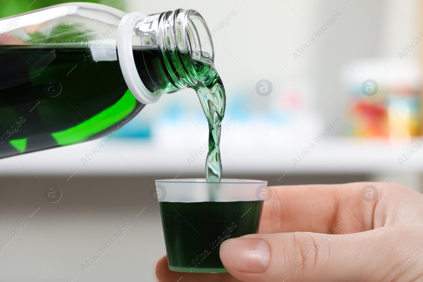 Photo of Woman pouring syrup from bottle into measuring cup against blurred background, closeup. Cold medicine