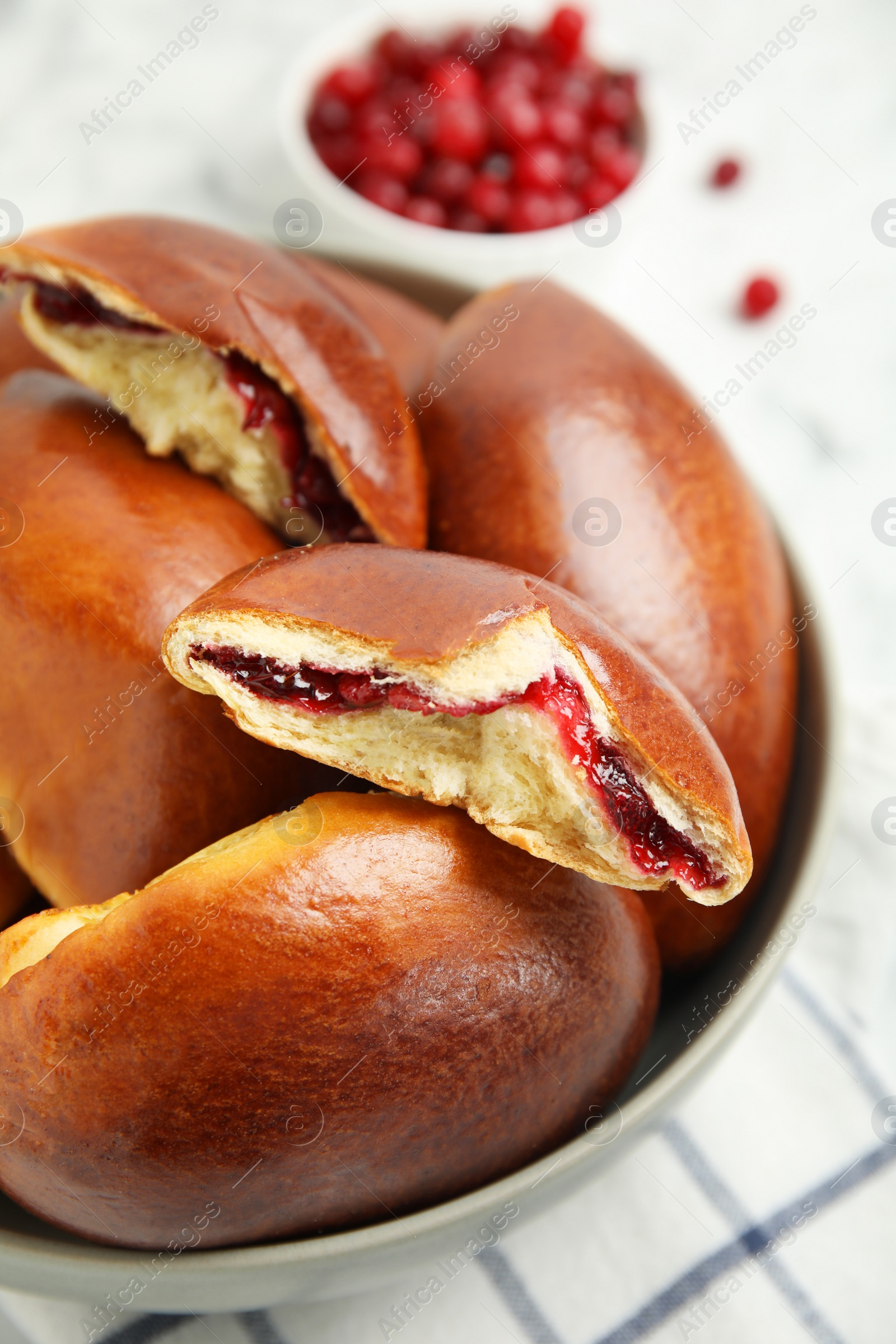 Photo of Delicious baked cranberry pirozhki in bowl on white table