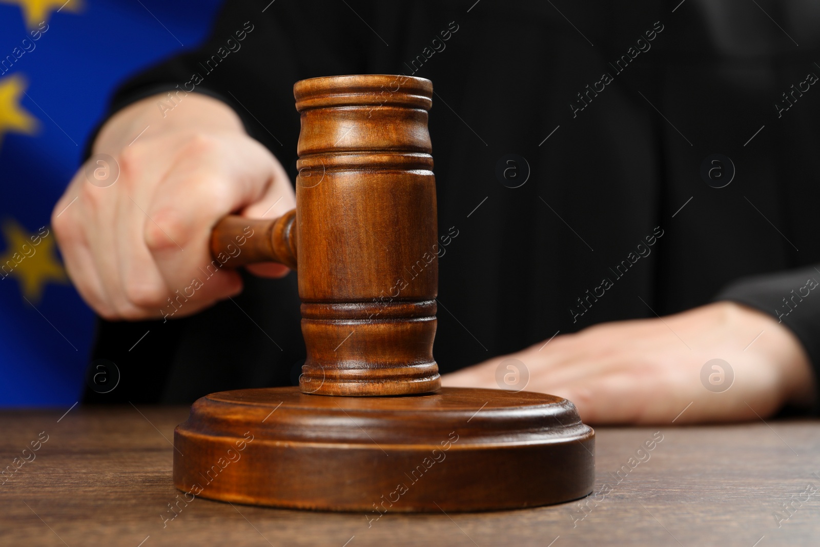 Photo of Judge with gavel at wooden table against flag of European Union, closeup