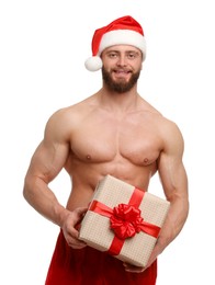 Attractive young man with muscular body in Santa hat holding Christmas gift box on white background