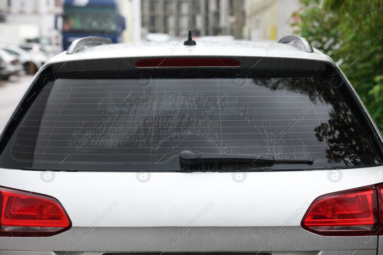 Photo of Wiper cleaning raindrops from car rear windshield outdoors