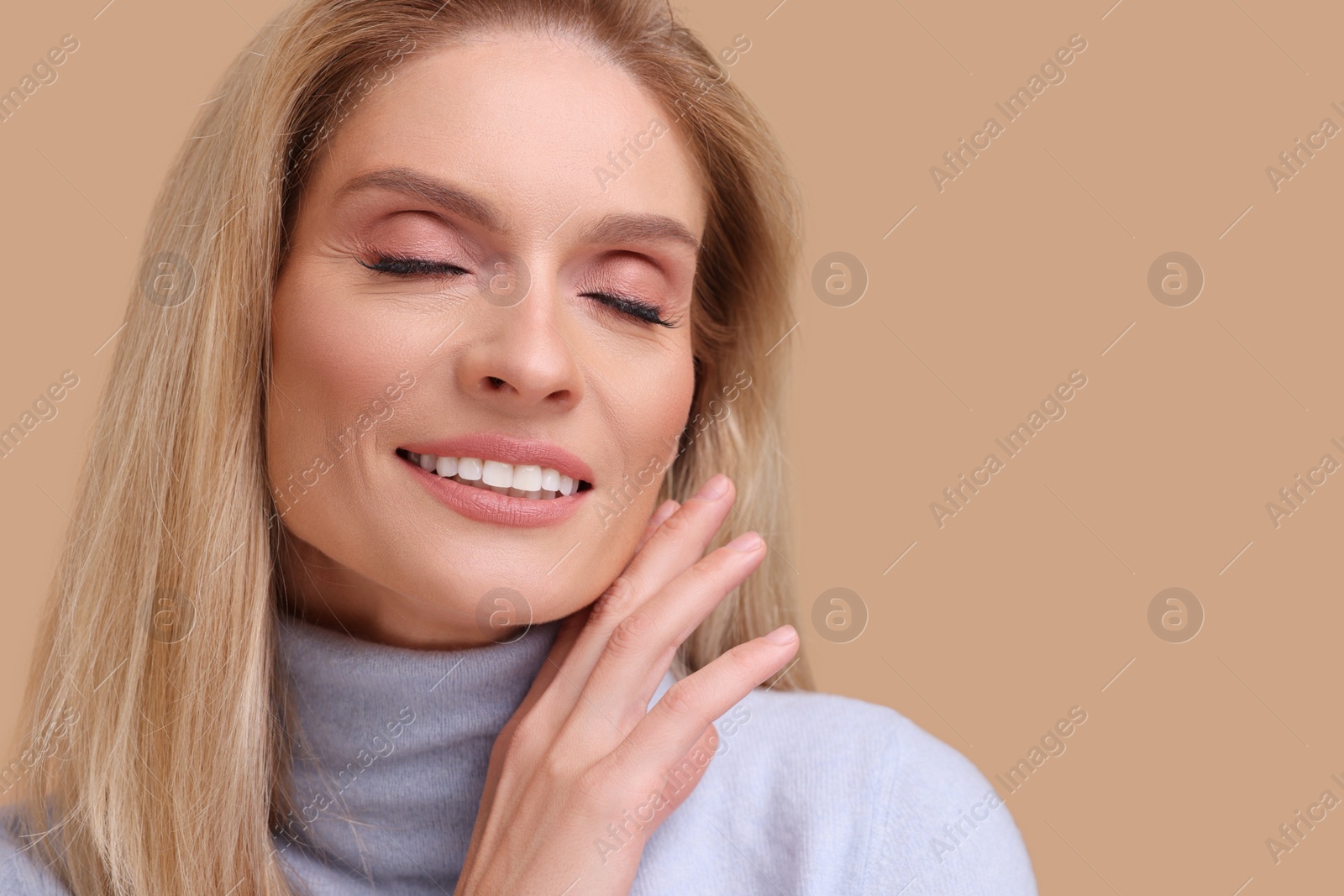 Photo of Portrait of smiling middle aged woman with blonde hair on beige background. Space for text