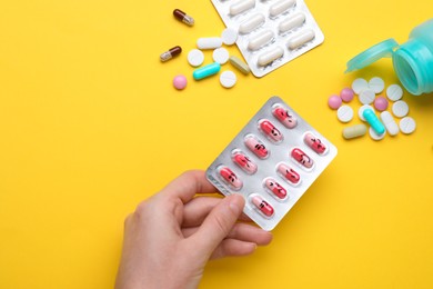 Photo of Woman holding colorful antidepressants with different emoticons on yellow background, top view
