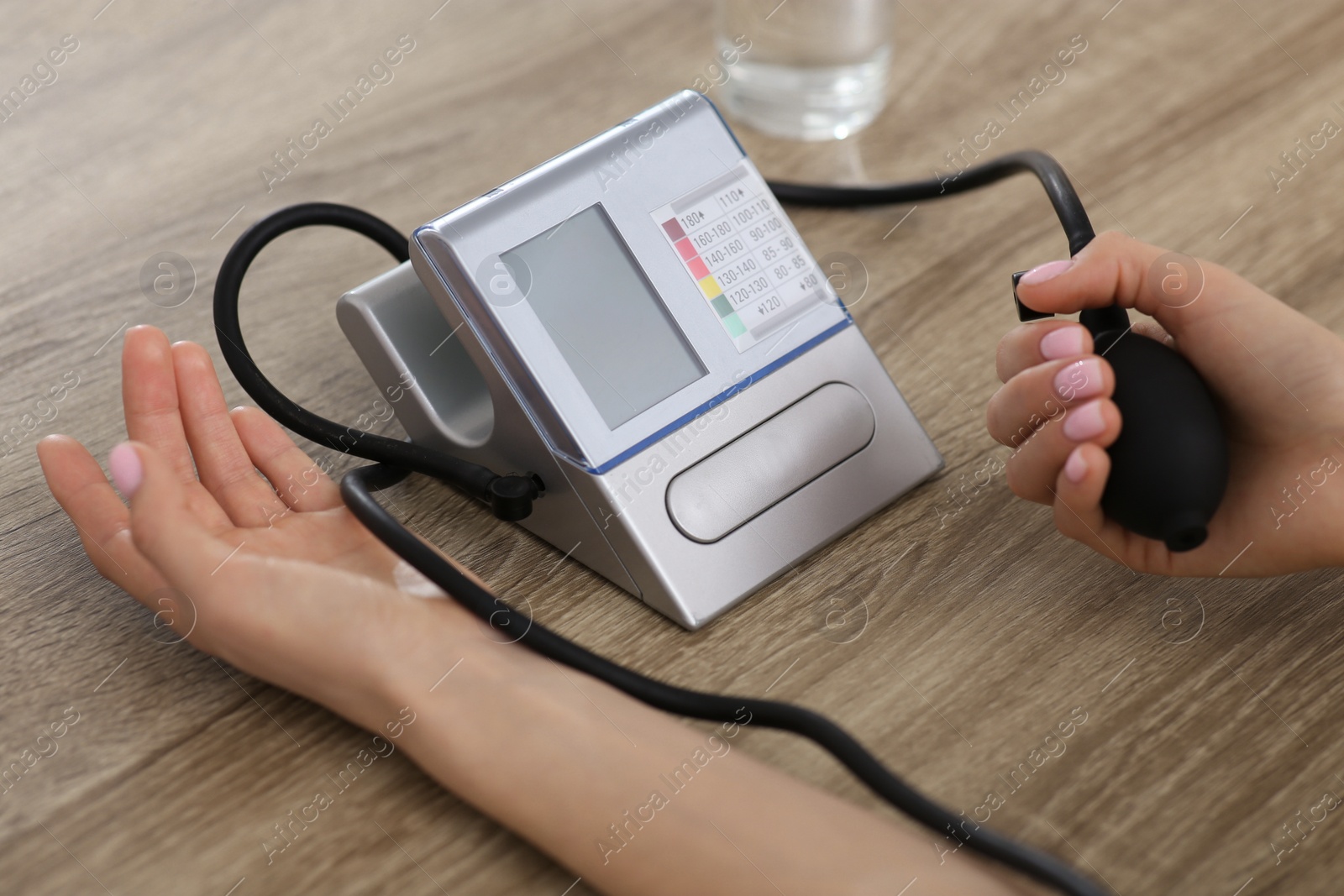 Photo of Woman checking blood pressure at wooden table indoors, closeup