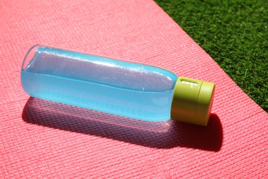 Bottle of light blue drink and mat on green grass