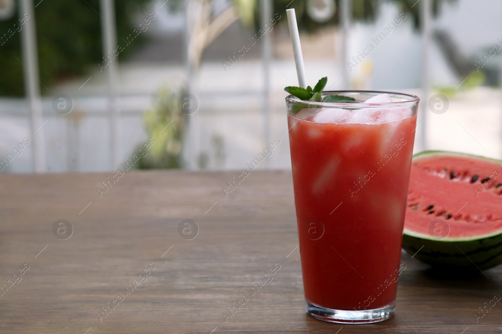 Photo of Glass of delicious watermelon drink with mint, ice cubes and fresh cut fruit on wooden table outdoors, space for text