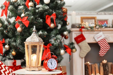 Lantern and alarm clock on table near decorated Christmas tree in stylish living room interior