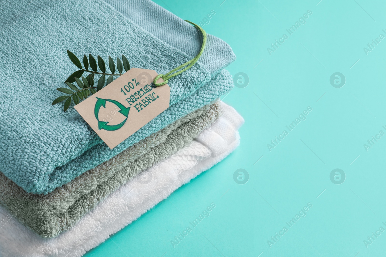Photo of Stacked towels with recycling label and plant on turquoise background, space for text