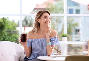 Photo of Young woman with glass of tasty healthy smoothie at table, indoors