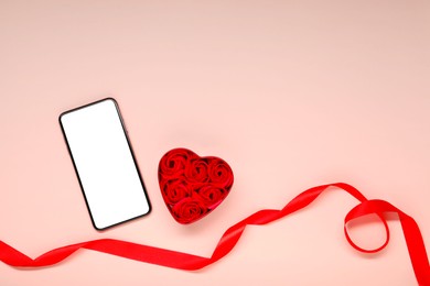 Long-distance relationship concept. Smartphone, decorative heart and red ribbon on beige background, flat lay with space for text