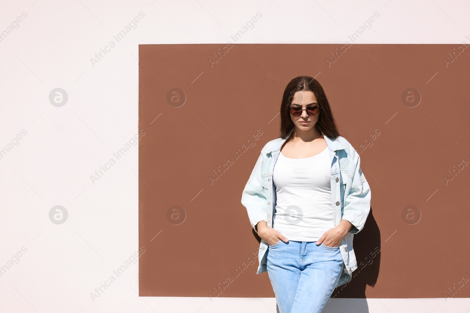 Photo of Young hipster woman in stylish jeans and jacket posing near color wall