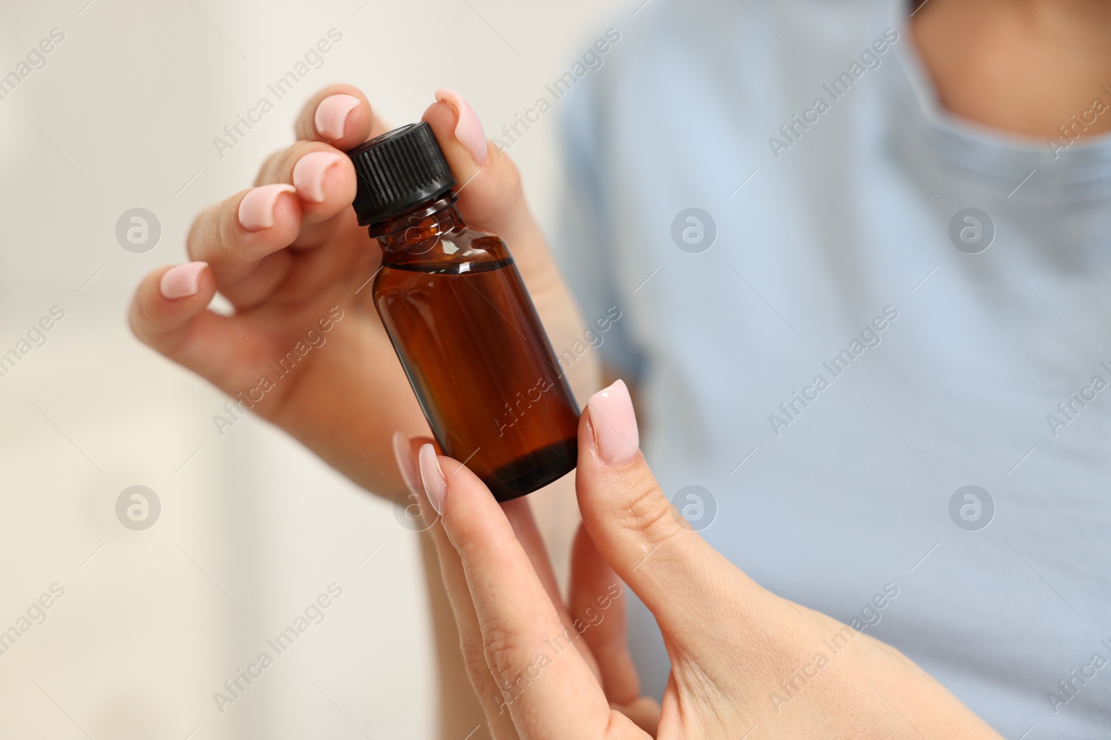 Photo of Aromatherapy. Woman with bottle of essential oil on light background, closeup