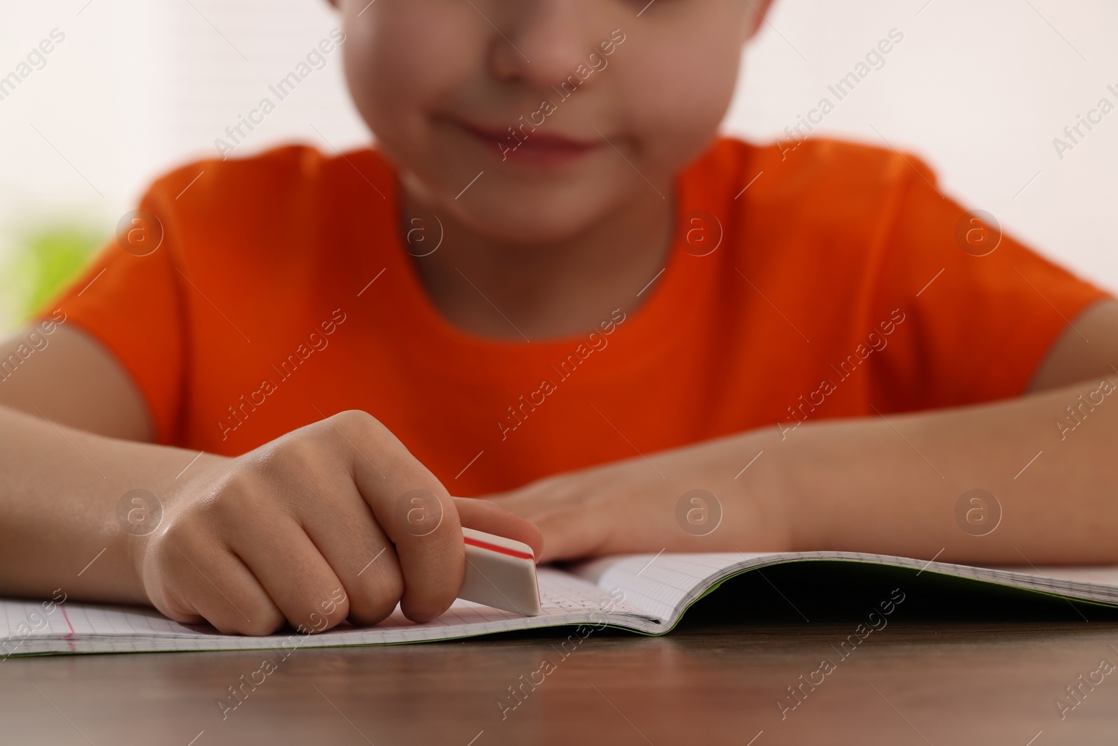 Photo of Little boy erasing mistake in his notebook at wooden desk, closeup