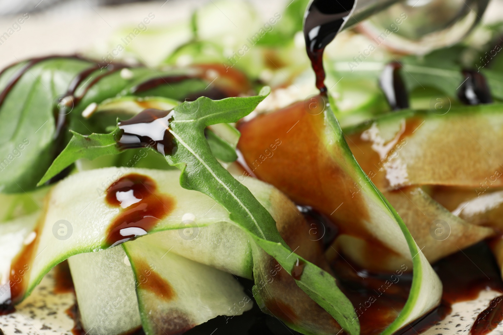 Photo of Pouring balsamic vinegar onto vegetable salad, closeup