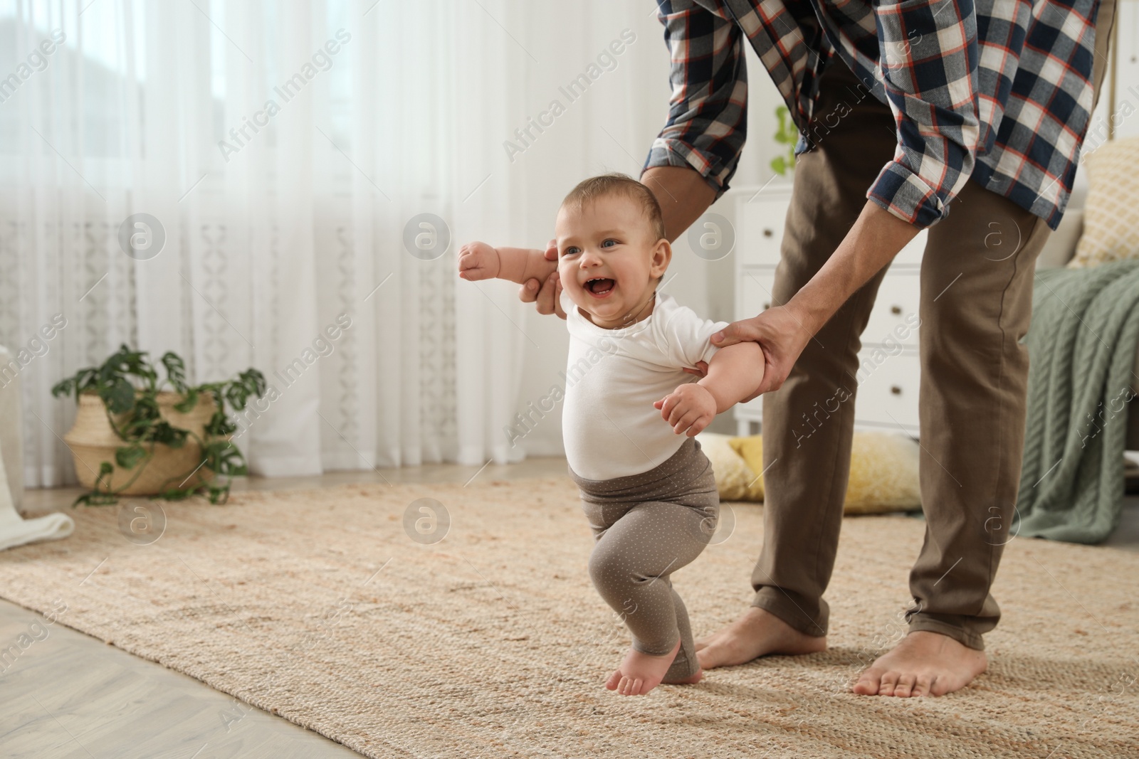 Photo of Father supporting his baby daughter while she learning to walk at home