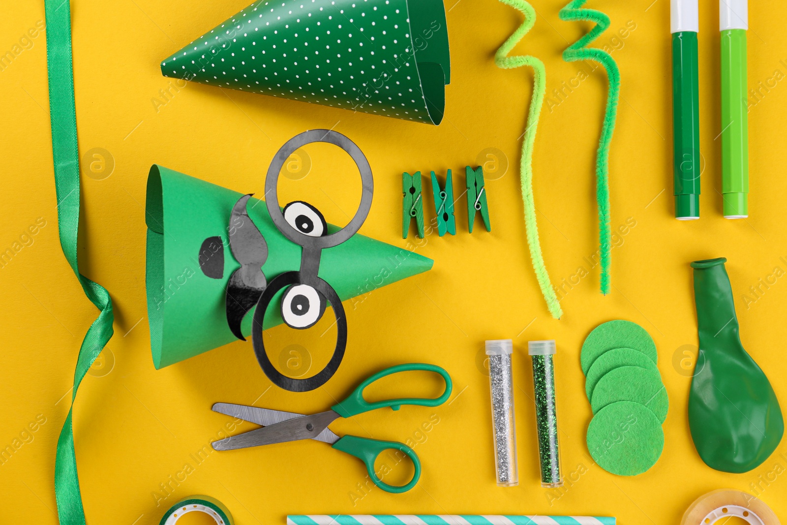 Photo of Handmade party hats and tools on yellow background, flat lay