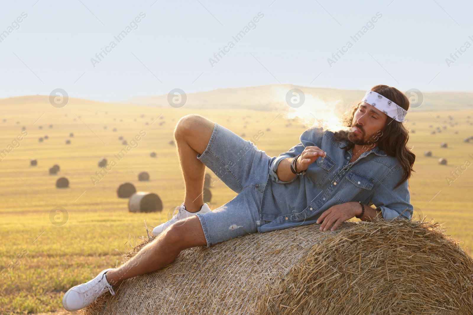 Photo of Hippie man smoking joint on hay bale in field