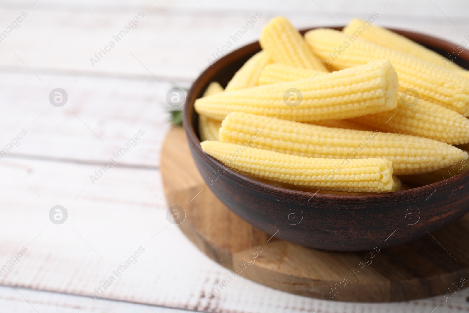 Photo of Tasty fresh yellow baby corns in bowl on white wooden table, closeup. Space for text