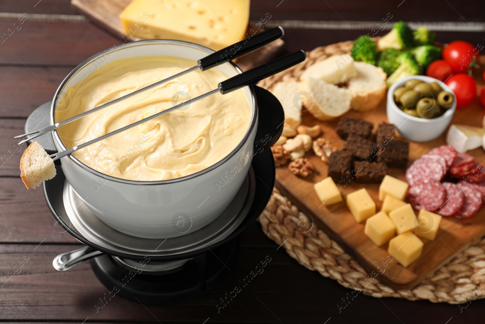 Photo of Fondue with tasty melted cheese, forks and different snacks on wooden table