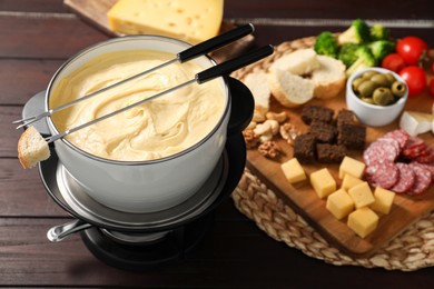 Photo of Fondue with tasty melted cheese, forks and different snacks on wooden table