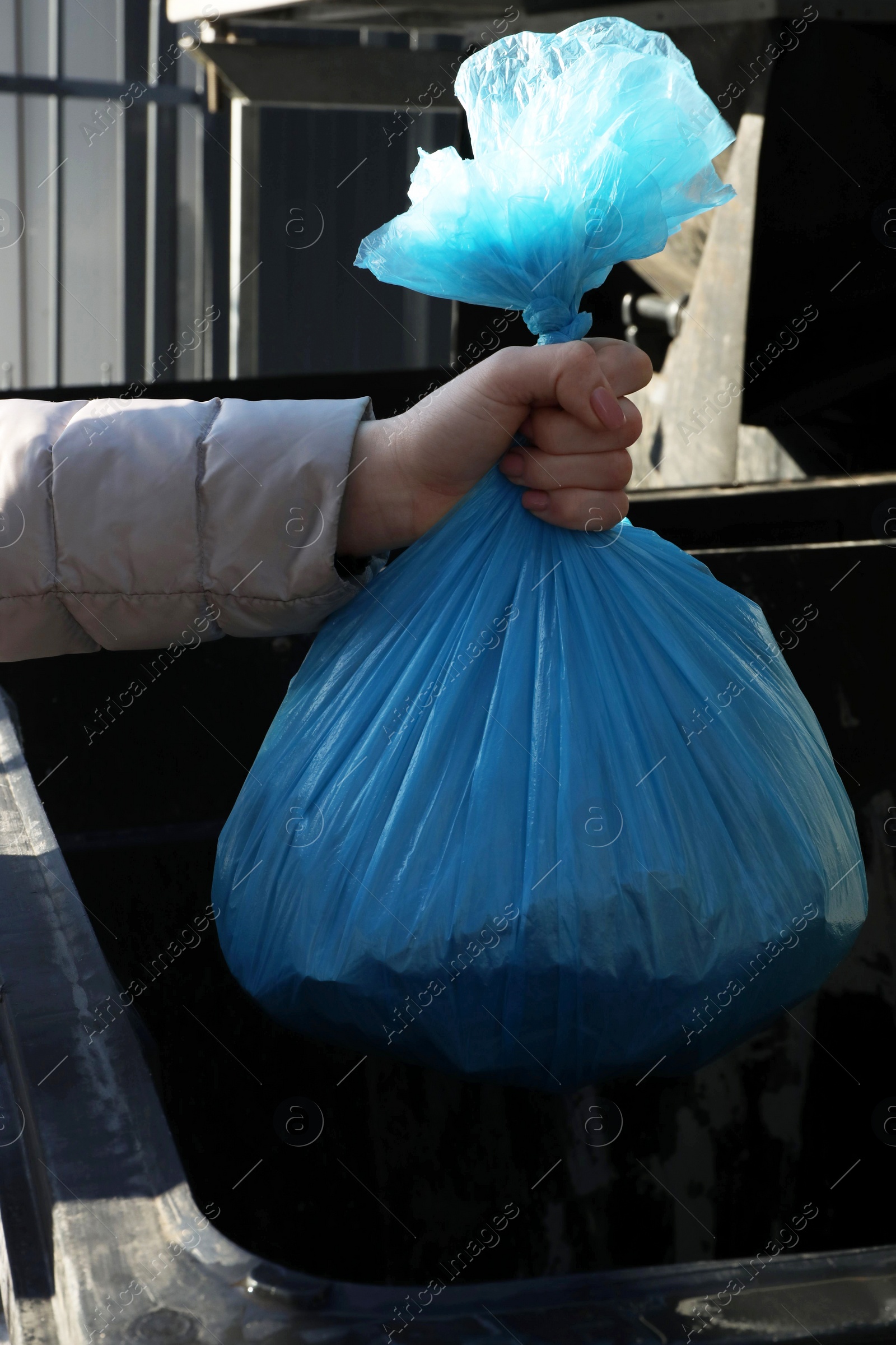 Photo of Woman throwing trash bag full of garbage in bin outdoors, closeup