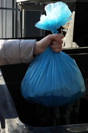 Woman throwing trash bag full of garbage in bin outdoors, closeup