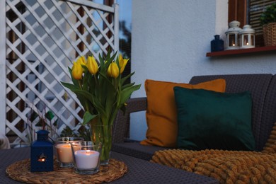 Photo of Soft pillows, blanket, burning candles and yellow tulips on rattan garden furniture outdoors