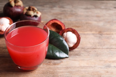 Delicious mangosteen juice in glass on wooden table. Space for text