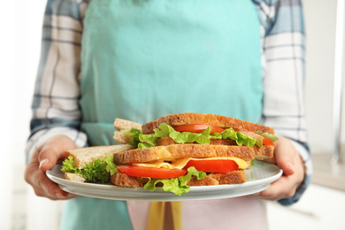 Woman holding plate with tasty sandwiches indoors, closeup