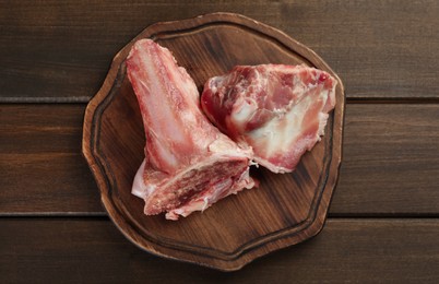 Photo of Cutting board with raw chopped meaty bones on wooden table, top view