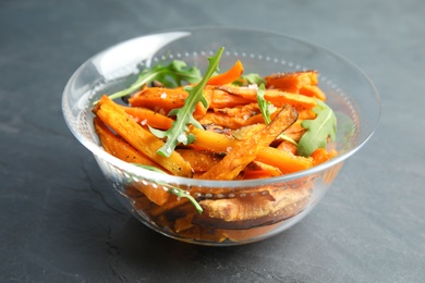 Glass bowl with baked sweet potato slices and arugula on grey background