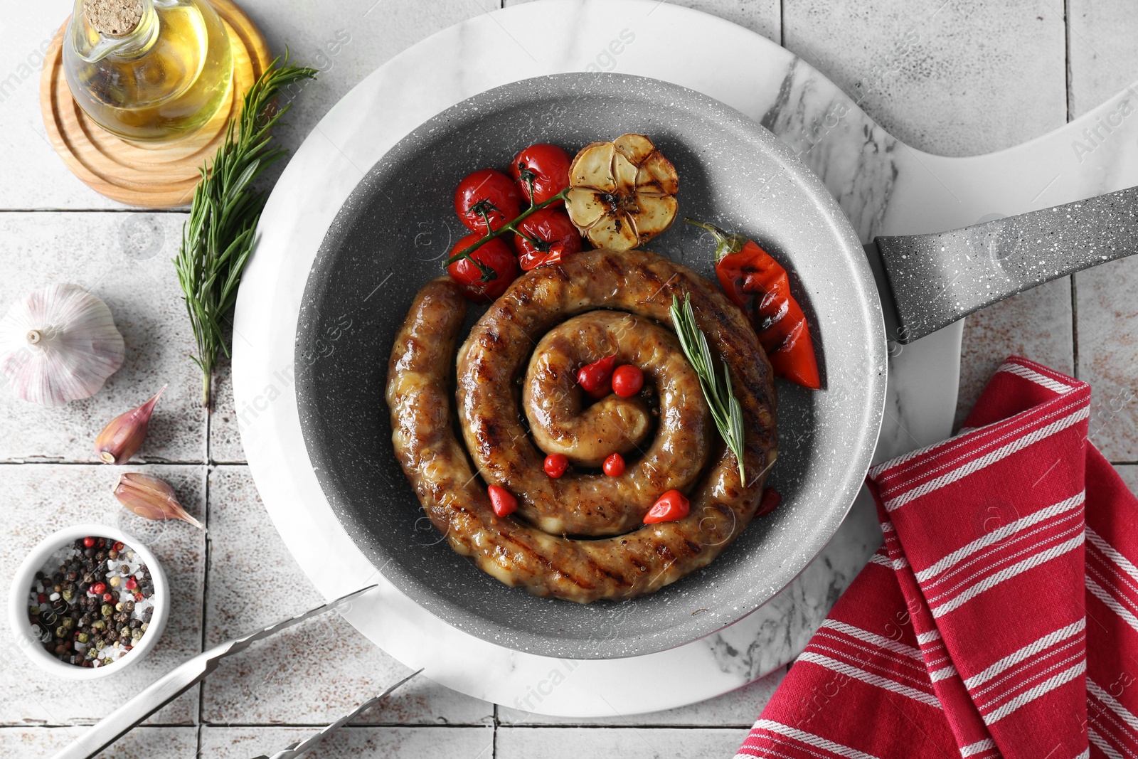 Photo of Delicious homemade sausage with garlic, tomatoes, rosemary and chili served on light tiled table, flat lay