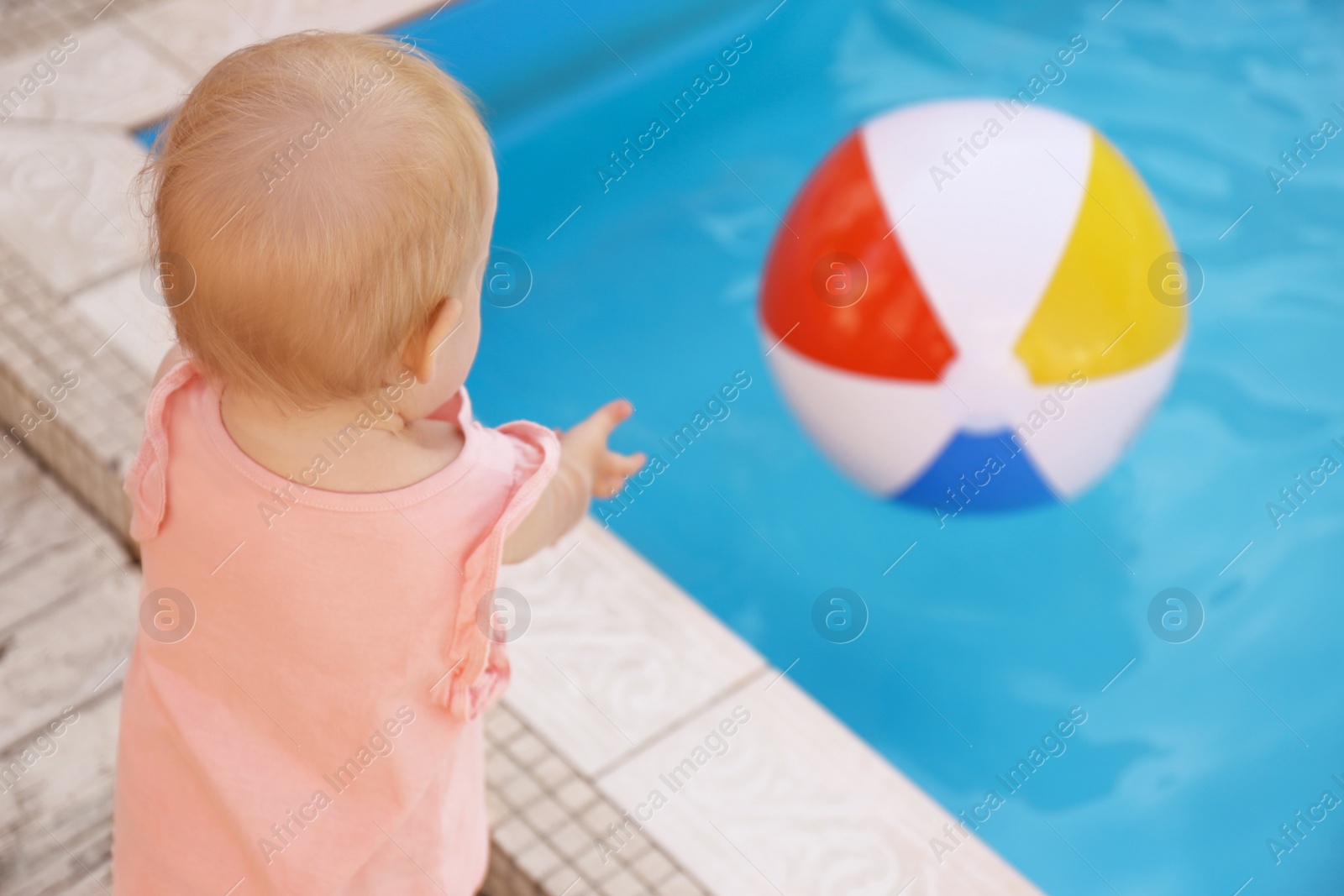 Photo of Little baby reaching for inflatable ball at outdoor swimming pool. Dangerous situation