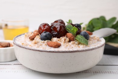 Photo of Tasty wheat porridge with milk, dates, blueberries and almonds in bowl on light wooden table, closeup