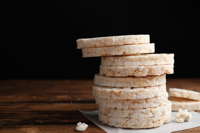 Photo of Stack of puffed rice cakes on wooden table against black background. Space for text
