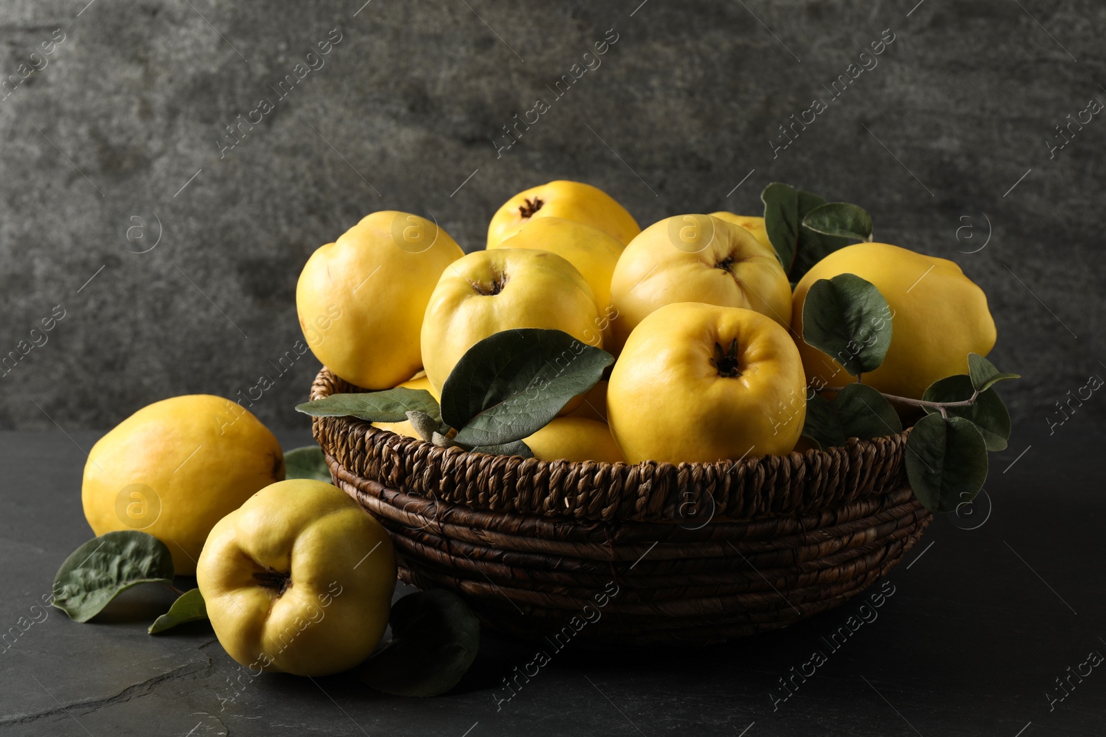 Photo of Fresh ripe organic quinces with leaves in wicker basket on black table