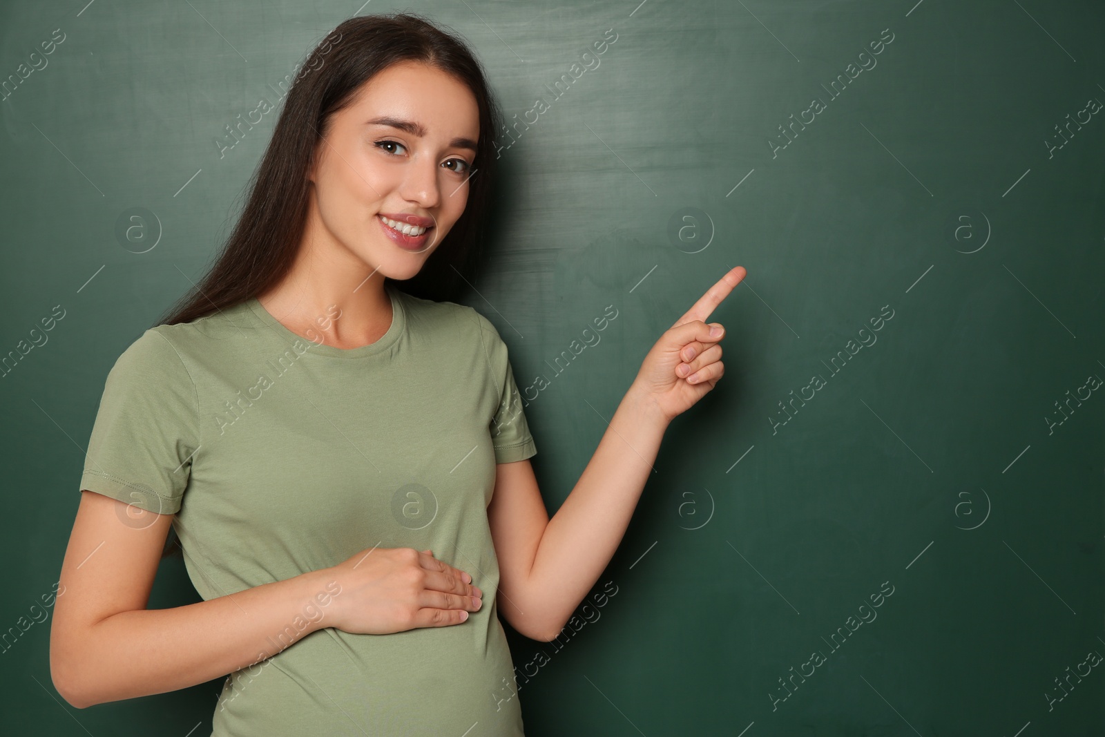 Photo of Pregnant woman near empty green chalkboard, space for text. Choosing name for baby