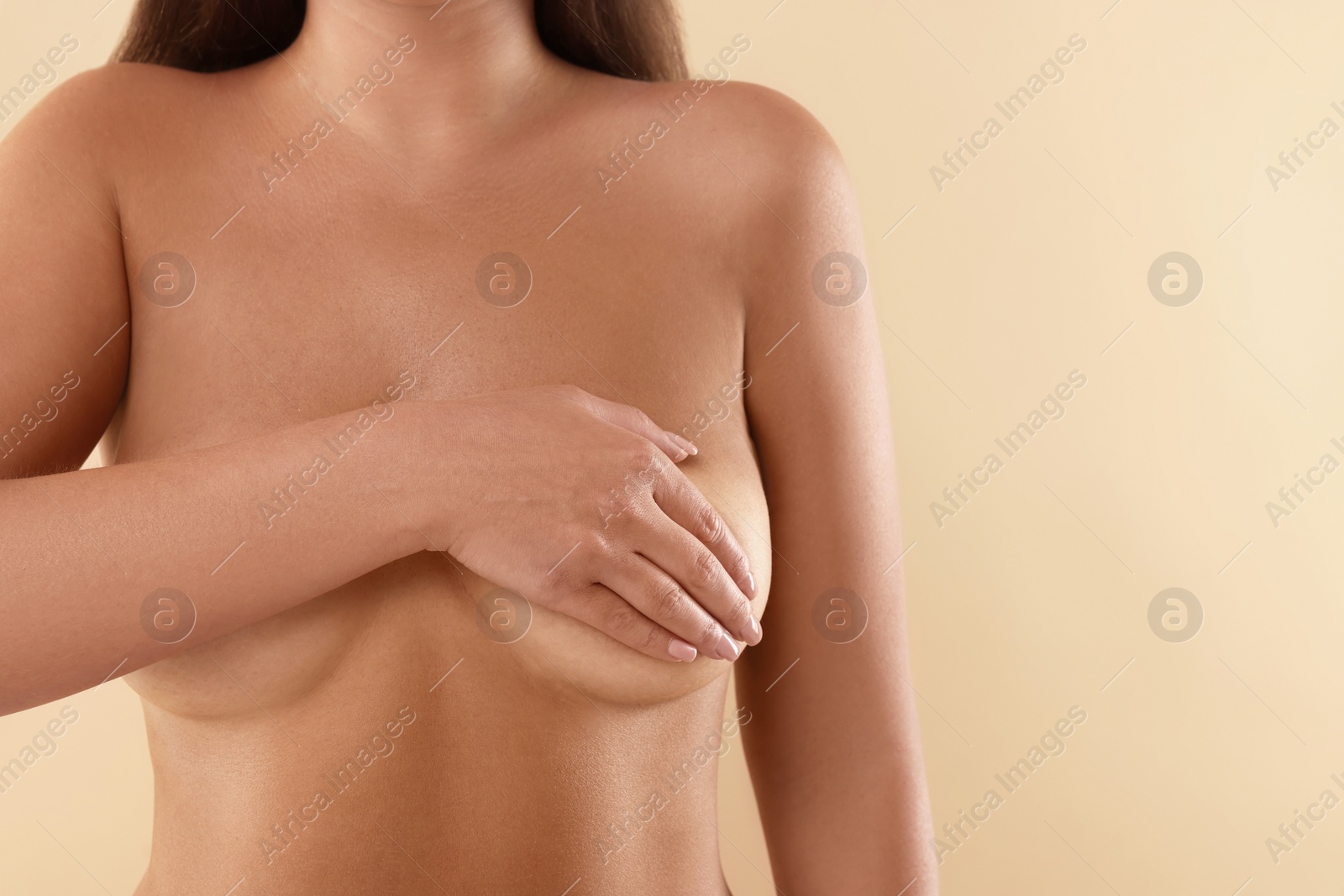 Photo of Naked woman covering her breast on beige background, closeup. Space for text