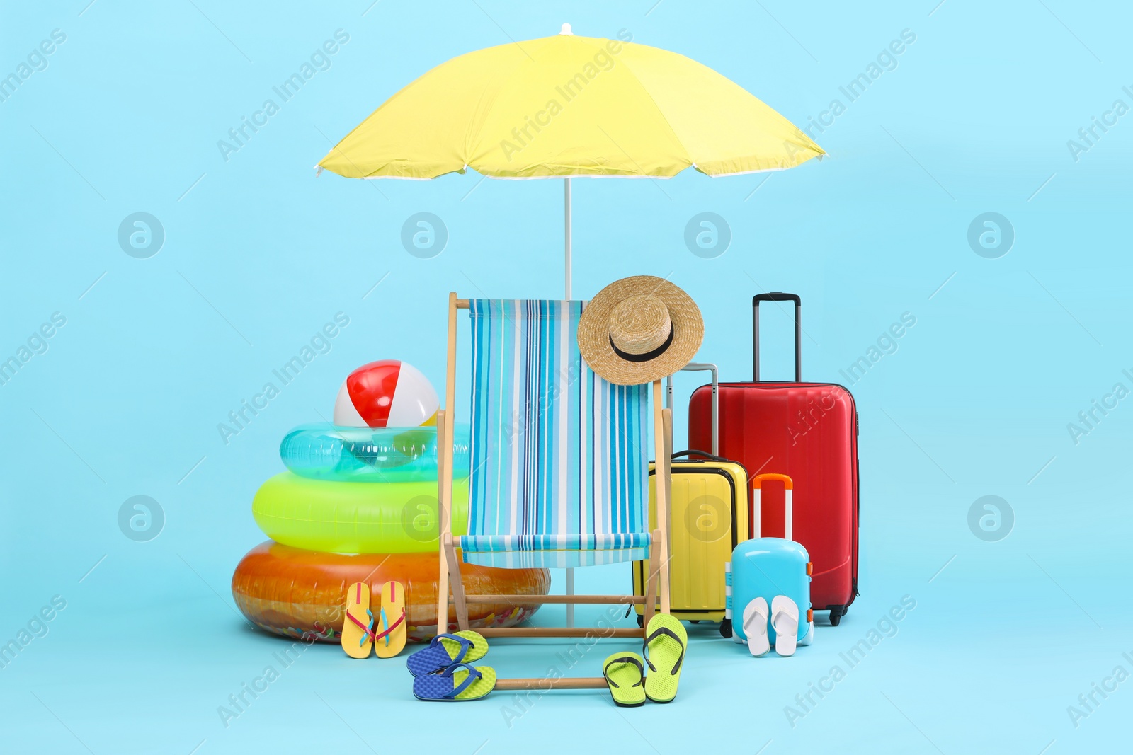 Deck chair, umbrella, suitcases and beach accessories on light blue background. Summer vacation Photo of Deck chair, umbrella, suitcases and beach accessories on light blue background. Summer vacation