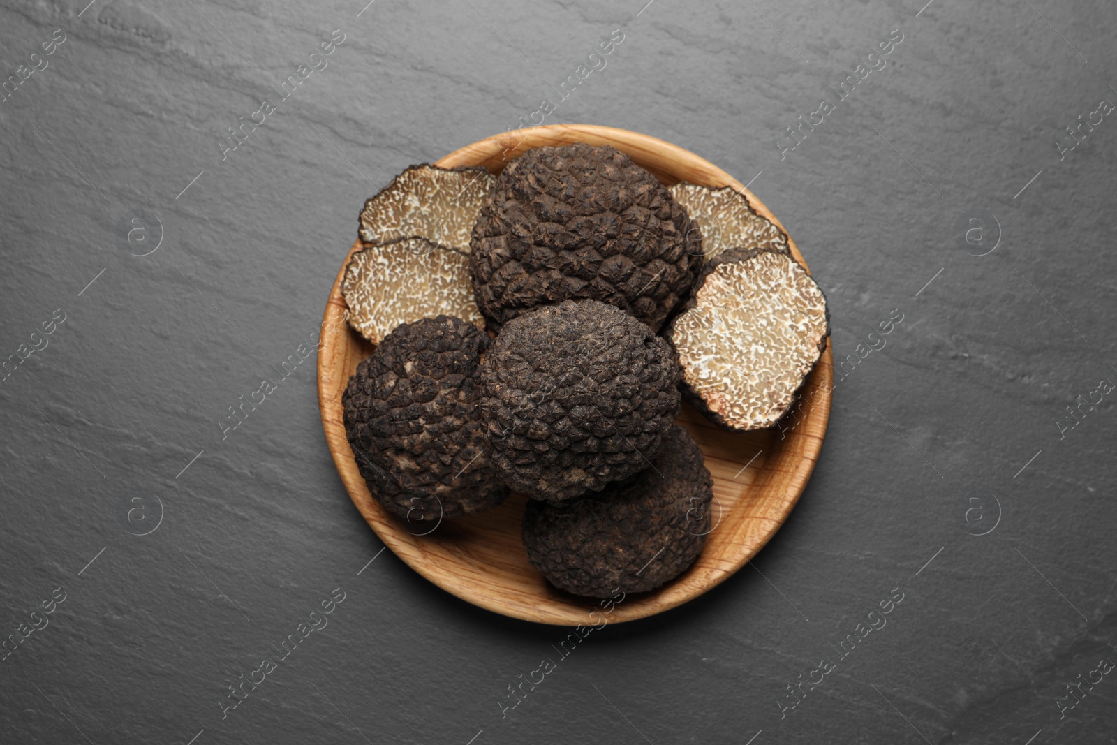 Photo of Black truffles in wooden plate on grey table, top view