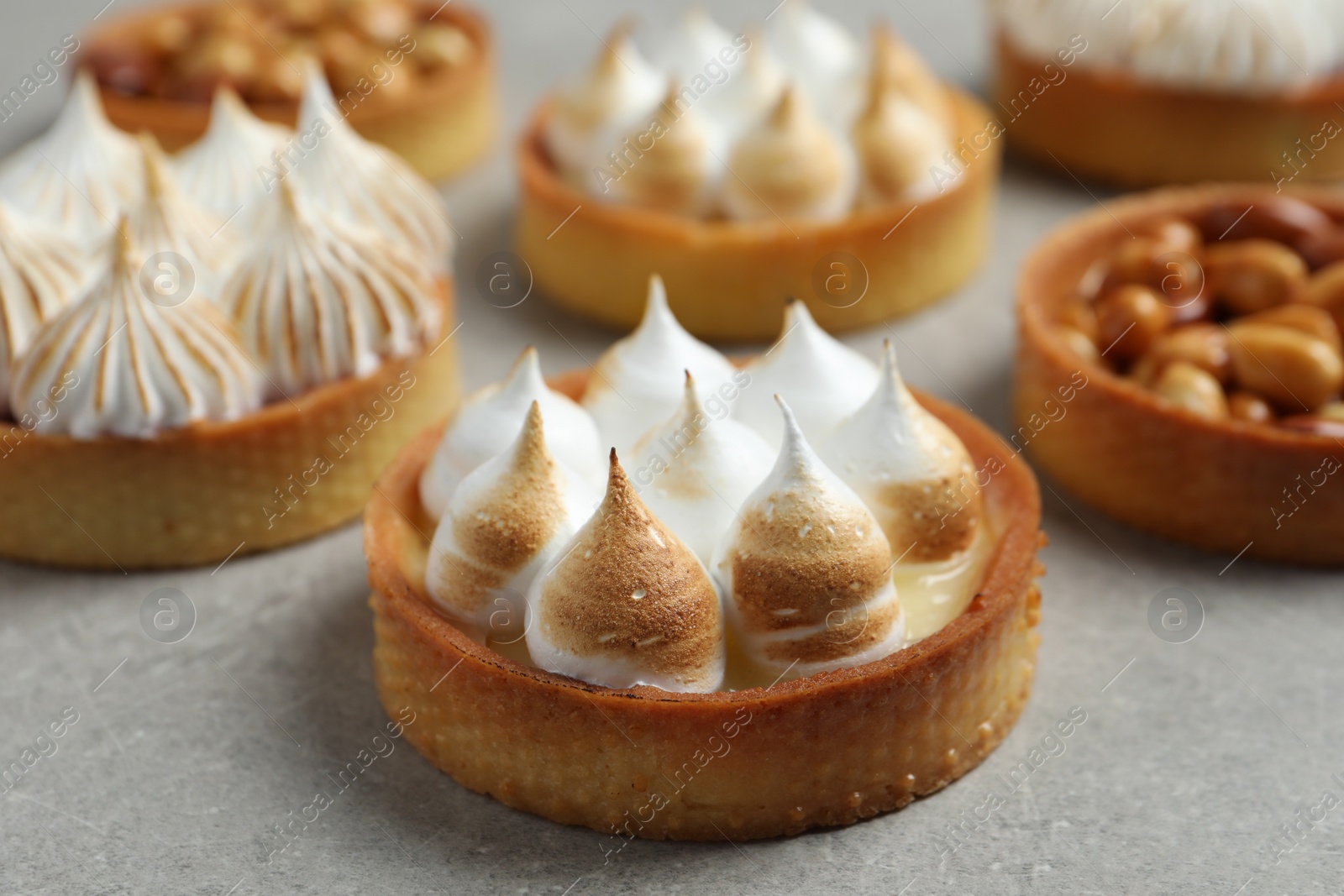 Photo of Many different tartlets on grey table, closeup. Delicious dessert