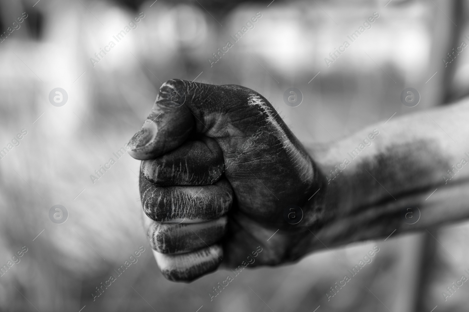 Photo of Dirty worker clenching fist on blurred background, closeup of hand. Black and white effect